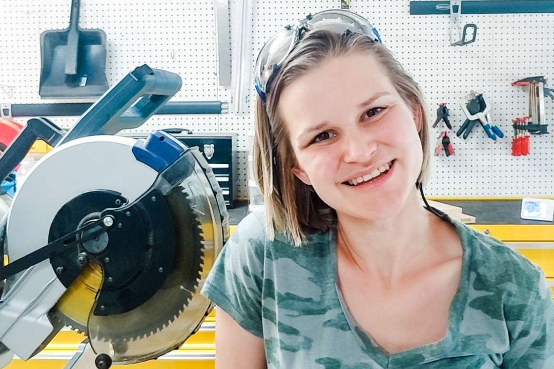 Emilee Anderson, blogger, poses with a saw and other tools in a woodworking workshop