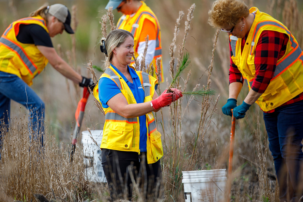 Two women in safety vests work together to plant a Rayonier pine tree by hand