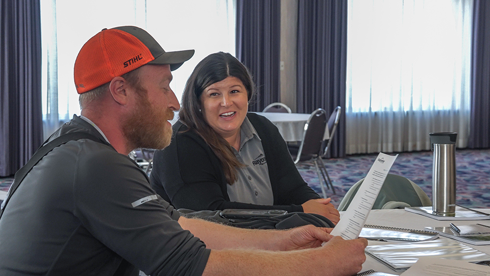 A logger and Tracie sit at a table together in a conference room.