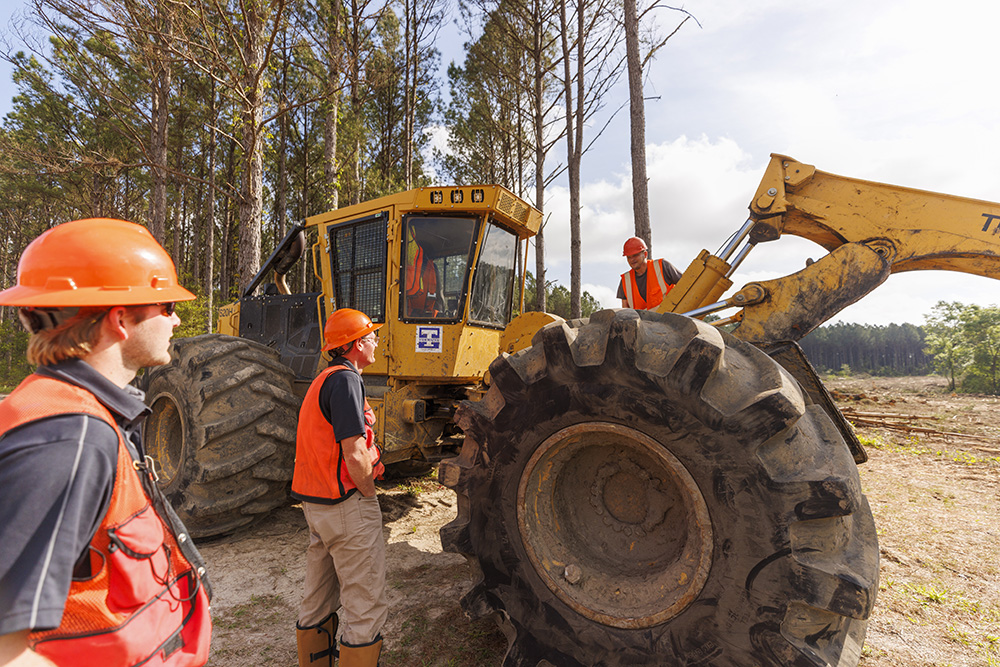 Phillip stands next to skidder and talks to operator in the woods.