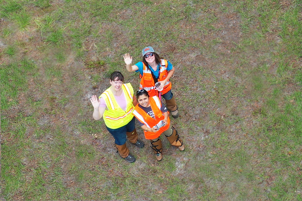 Three women standing together while one holds drone controller