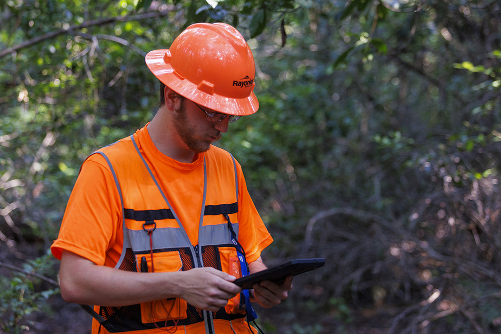 Man in high vis gear looks at a tablet he is holding